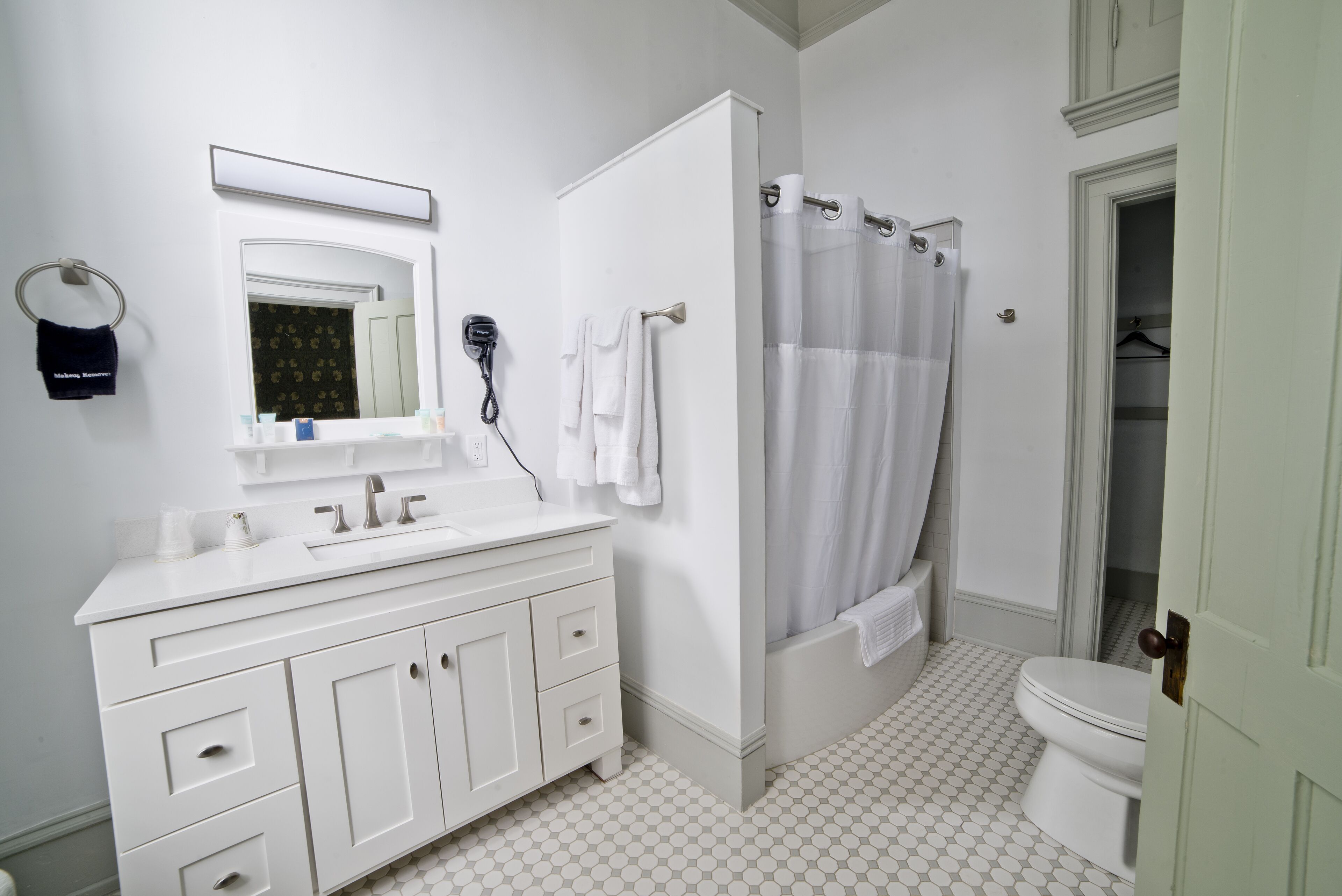 Un baño con tocador blanco, espejo, cortina de ducha y retrete.