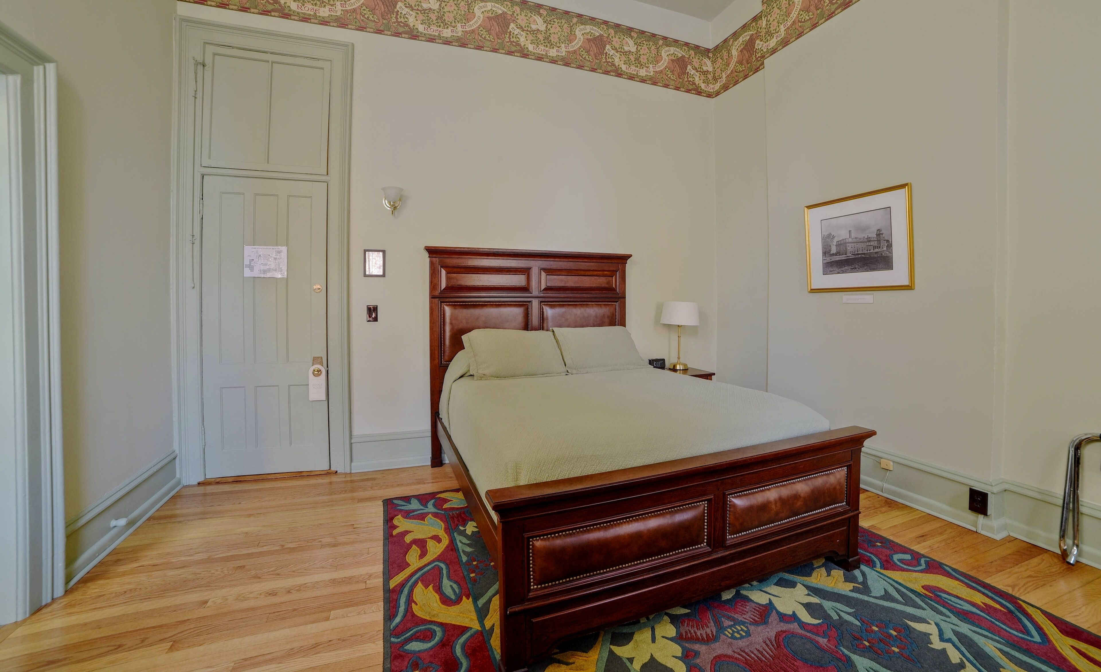 Une chambre à coucher bien rangée, avec un lit en bois, un tapis à motifs et un tableau encadré accroché au mur.