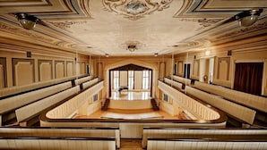 A grand hall with a central staircase, ornate ceiling, and rows of seating. - Oneida Community Mansion House (Oneida)