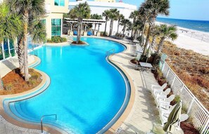 Ein Pool mit geschwungener Form, umgeben von Palmen und Liegestühlen, mit Blick auf Strand und Meer.