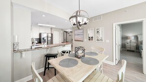 A modern kitchen with a central island, a dining area with a wooden table and chairs, and a hallway leading to a bedroom.