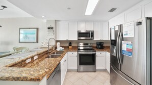 A modern kitchen with white cabinets, stainless steel appliances, granite countertops, and a dining area with a view.