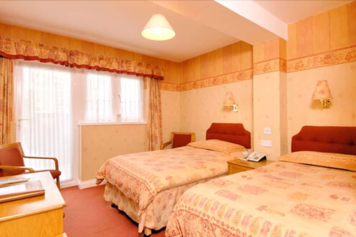 Ein Hotelzimmer mit zwei Betten, einem Schreibtisch, einem Stuhl und einem fenster mit Vorhängen.