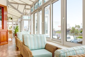 A sunlit room with wicker sofas, large windows, and a chandelier. - Marine Hotel Paignton (Paignton)