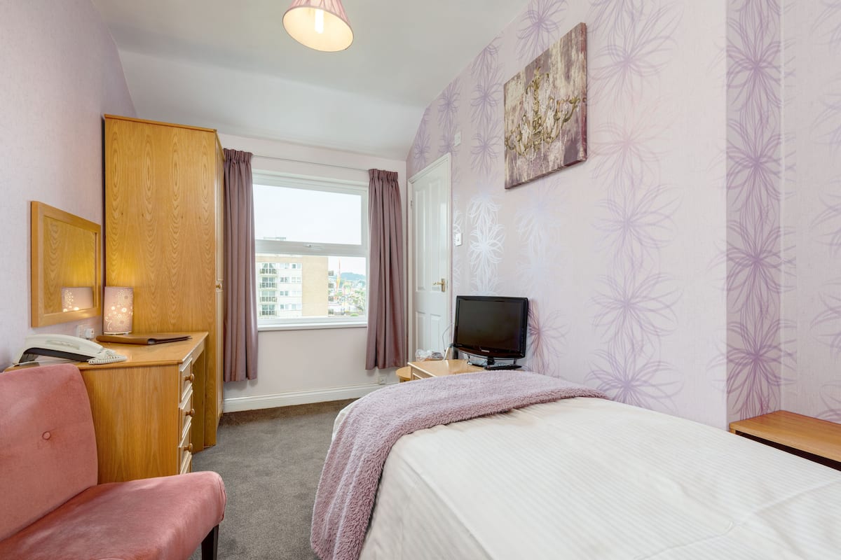 Ein Hotelzimmer mit einem Bett, einem Schreibtisch mit Telefon, einem Fernseher und einem Fenster mit Vorhängen.