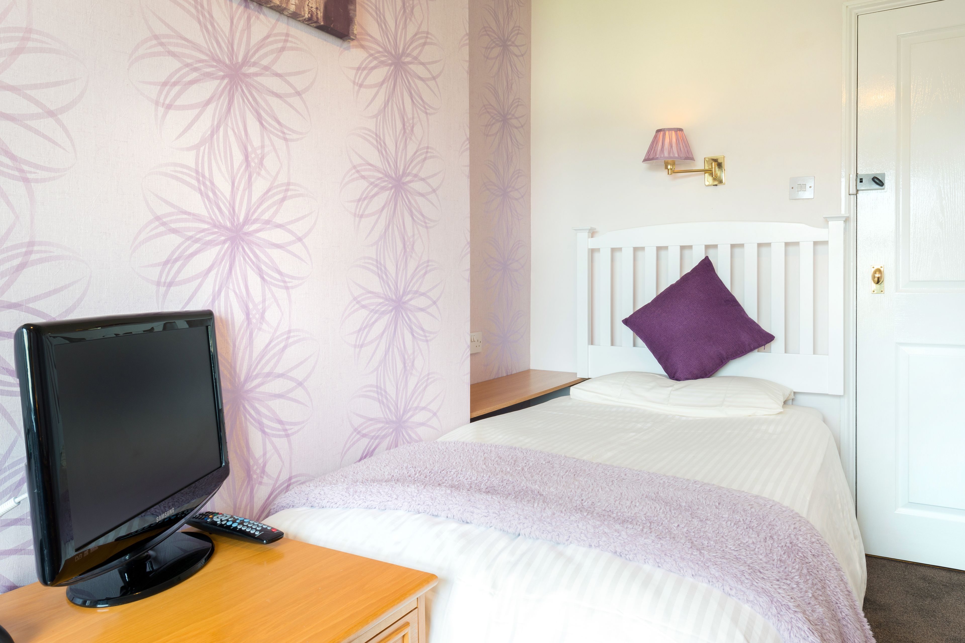 A bedroom with a bed, a TV on a wooden table, and a wall-mounted lamp.