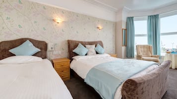 A hotel room with two beds, a large window with curtains, a chair, and a small table.