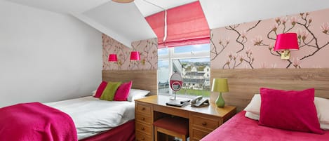 A bedroom with two beds, a desk, and a window with a view.