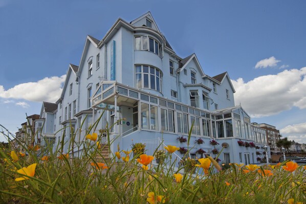 A large, light blue building with multiple windows and balconies, surrounded by yellow flowers. - Marine Hotel Paignton (Paignton)
