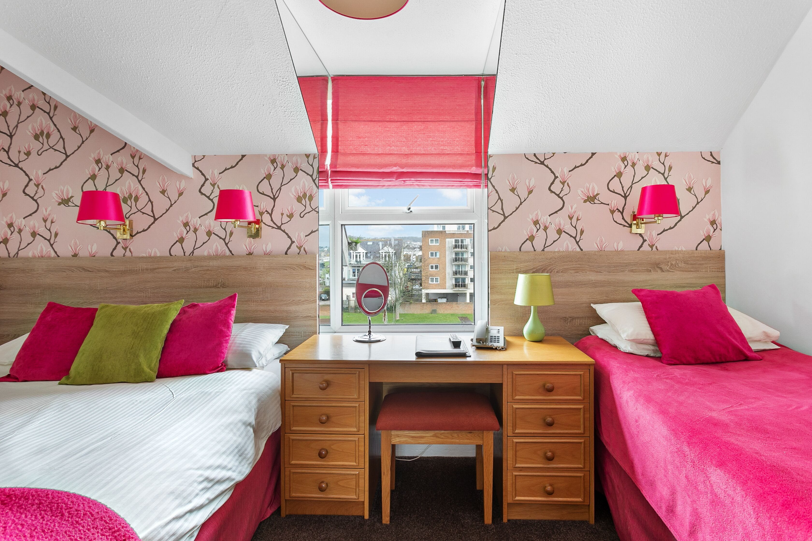 Une chambre d’hôtel avec deux lits, un bureau et une fenêtre donnant sur des immeubles.