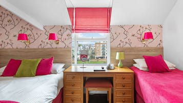 A hotel room with two beds, a desk, and a window with a view of buildings.