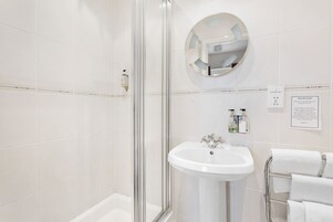 Un baño moderno con cabina de ducha de vidrio, un espejo redondo, lavamanos pedestal y un perchero para toallas.