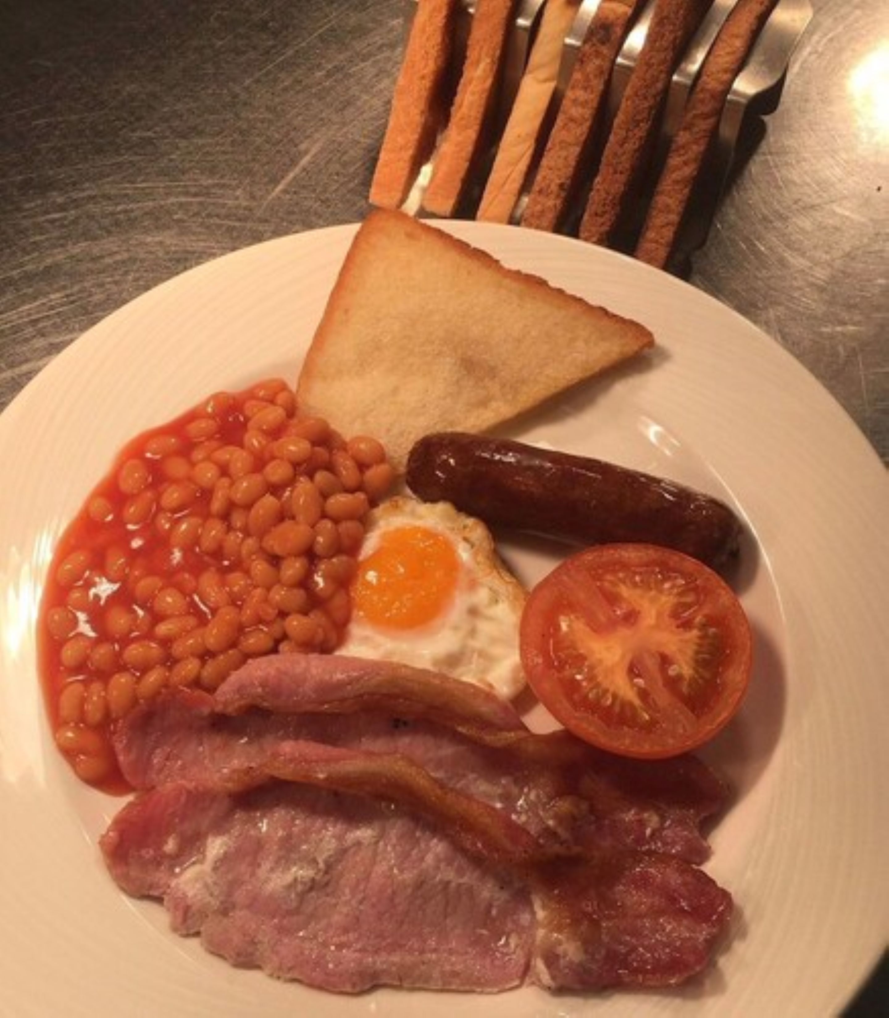 A plate with beans, sausage, bacon, a fried egg, toast, and a tomato.