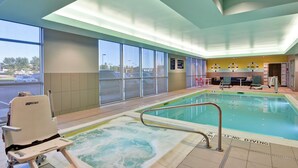 Zona de piscina de hotel con jacuzzi, sillas de descanso y vista al estacionamiento.