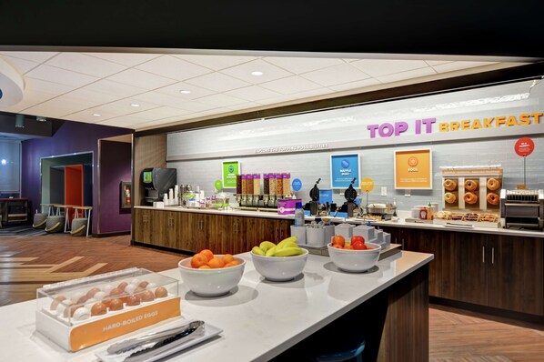 Un área de desayuno con un mostrador que exhibe diversas opciones de comida y un cartel que dice "TOP IT BREAKFAST".