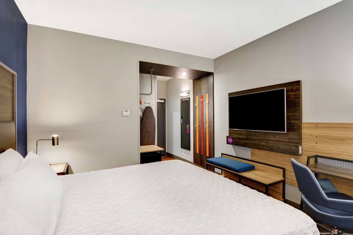 A hotel room with a large bed, a desk with a chair, a TV mounted on the wall, and a wardrobe with a mirror.