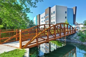 A wooden bridge over a calm water body with modern buildings in the background.