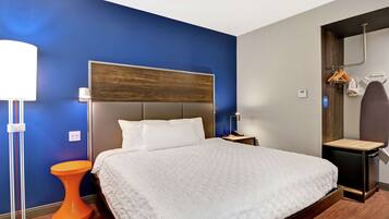 A hotel room with a large bed, a bedside table, a nightstand, a lamp, and a small orange stool.