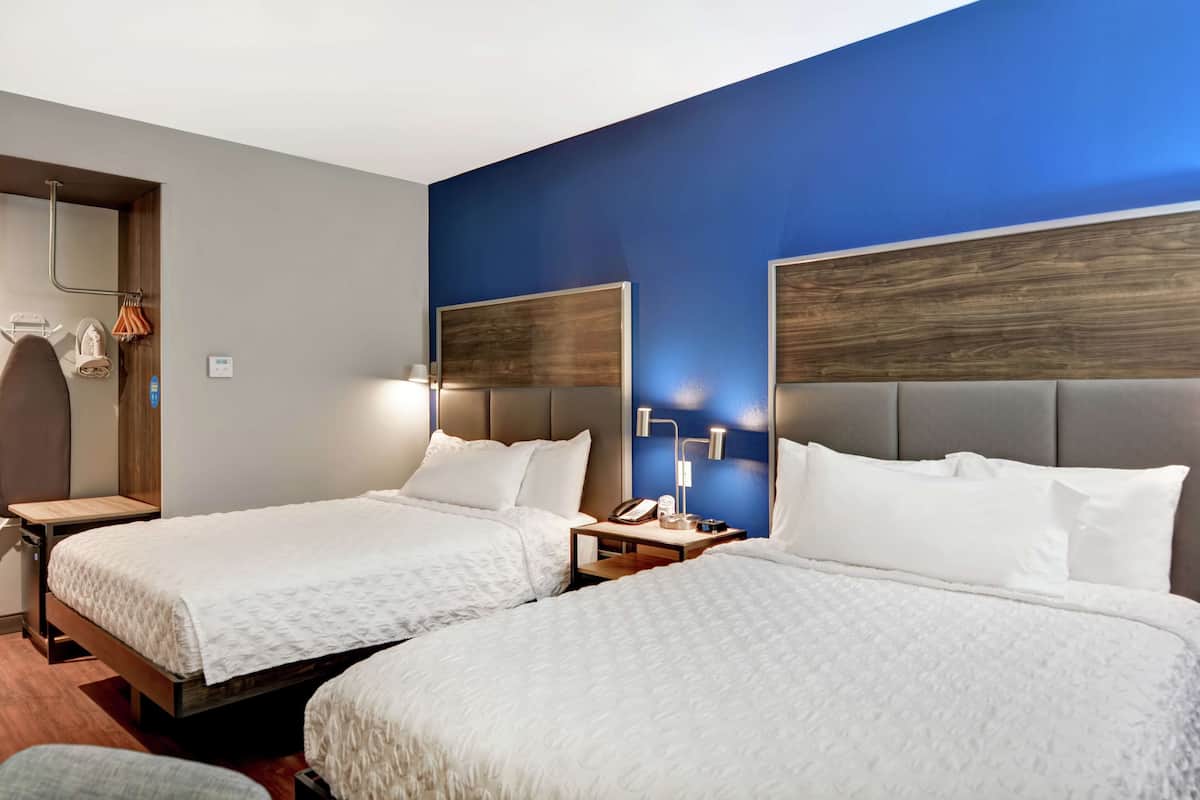 A hotel room with two beds, a wooden nightstand, a lamp, and a blue accent wall.