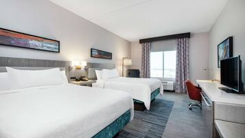A hotel room with two beds, a desk, a TV, and a window with curtains.