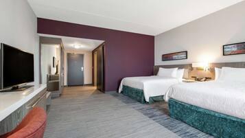 A hotel room with two beds, a TV, a desk, and a bathroom visible through an open door.