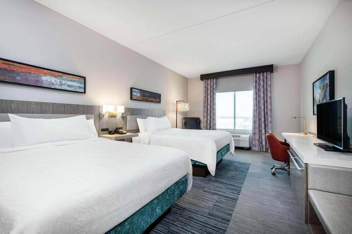 Ein Hotelzimmer mit zwei Betten, einem Schreibtisch, einem Fernseher und Bildern an den Wänden.
