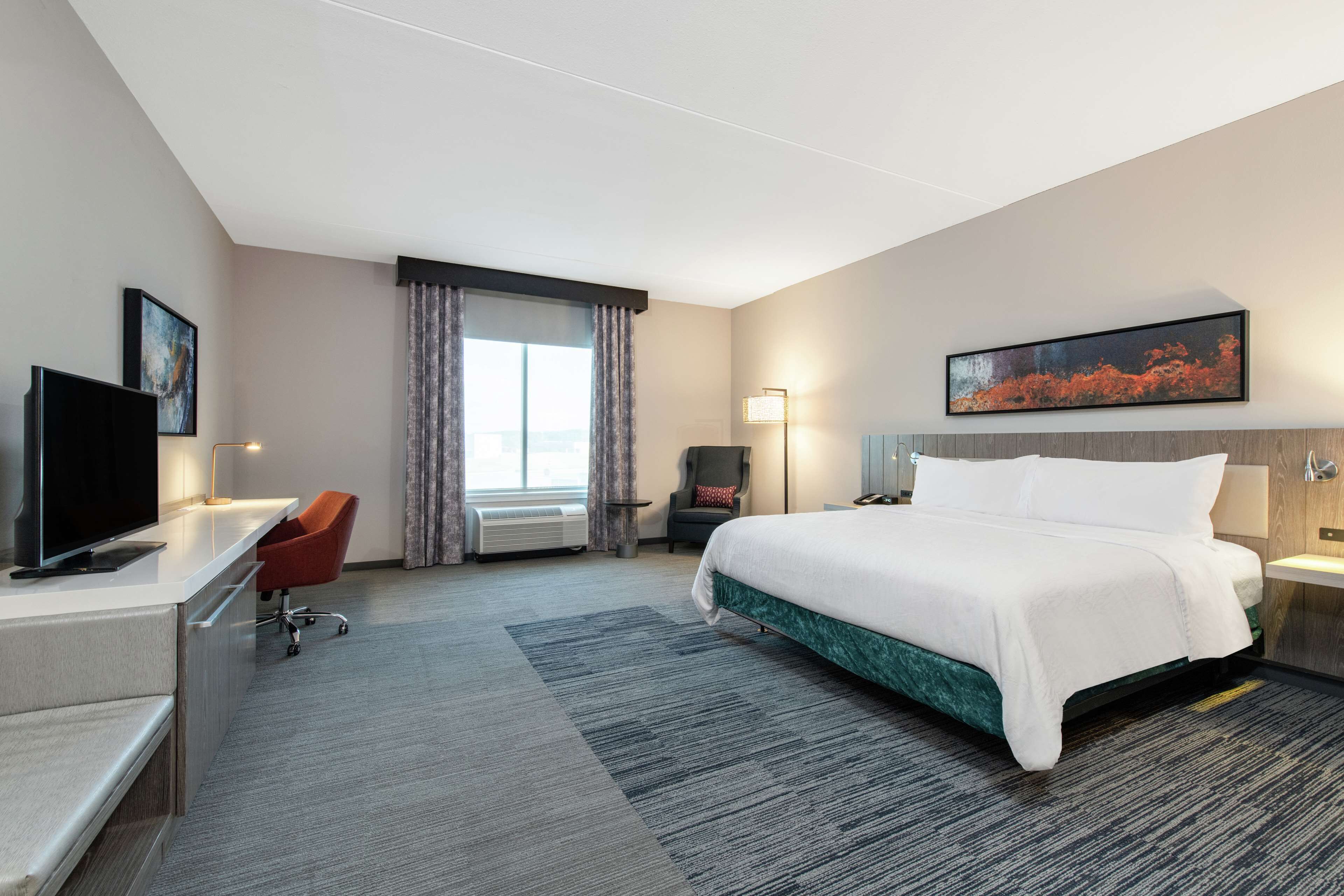 A hotel room with a bed, desk, chair, and a television.