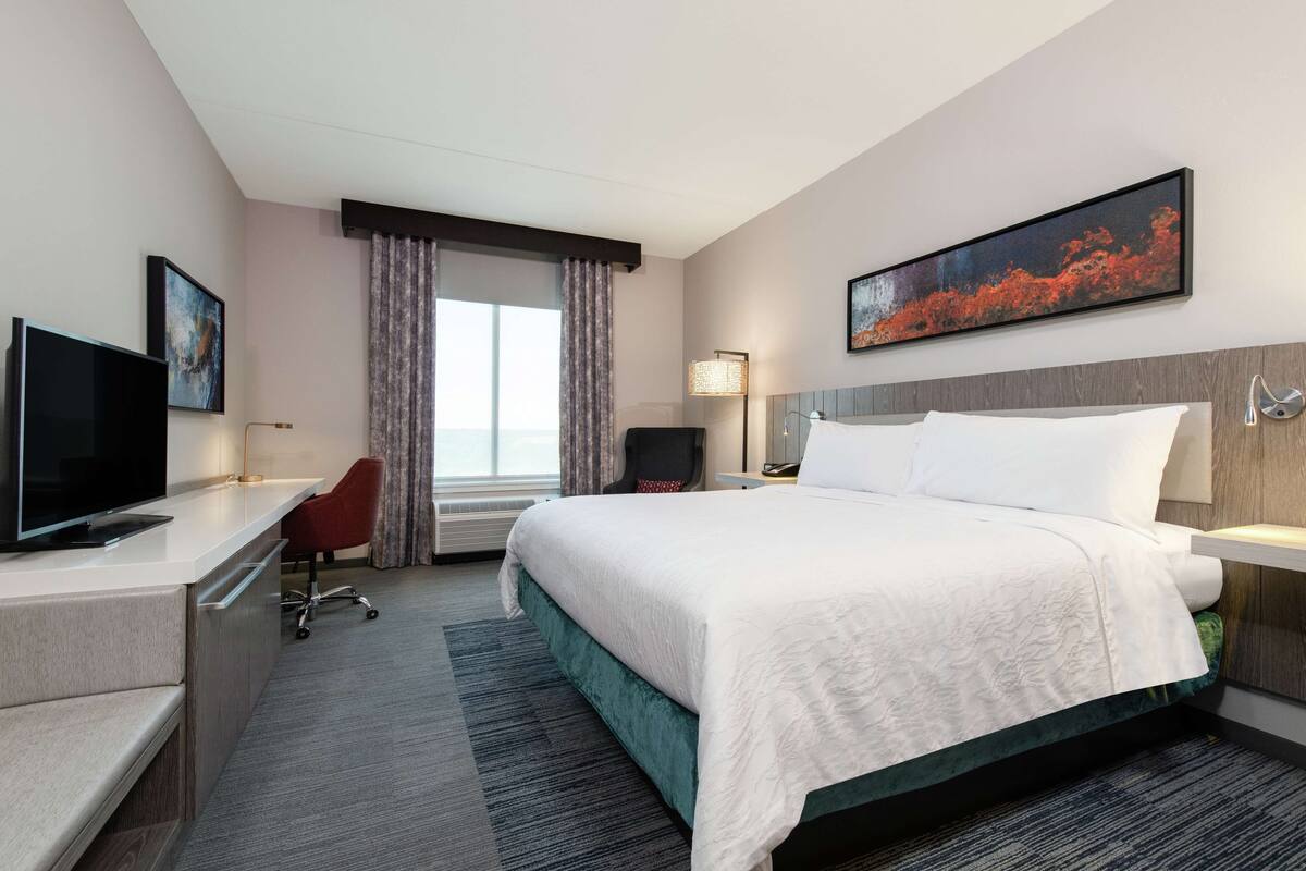 Ein Hotelzimmer mit Bett, Schreibtisch, Stuhl, Fernseher und einem Fenster mit Vorhängen.
