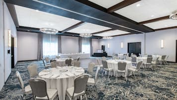 A conference room with round tables and chairs, a stage, and a large screen.