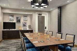 A conference room with a long table, chairs, a television, framed pictures on the wall, and a door with a unique design. - The Wilbur Lititz, Tapestry Collection by Hilton (Lititz)