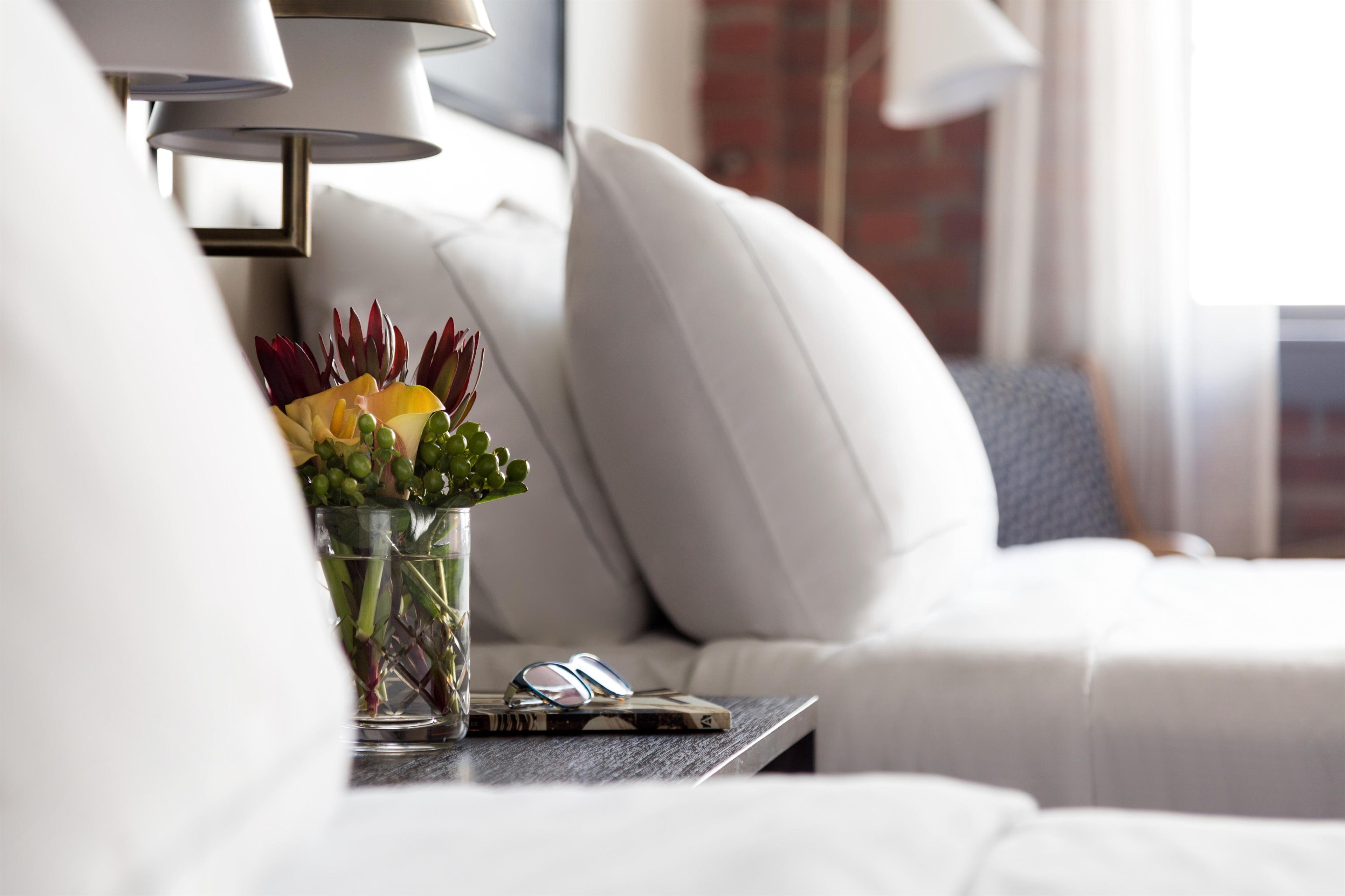 A modern living room with a sofa, a glass vase with flowers, a lamp, and a book.