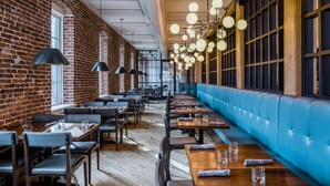 A restaurant with brick walls, wooden tables, and blue cushioned seating. - The Wilbur Lititz, Tapestry Collection by Hilton (Lititz)