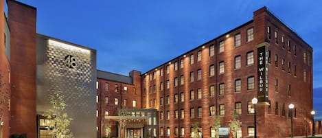 Un edificio de ladrillo de varios pisos con una entrada moderna, un gran número iluminado '48' en la fachada y un acceso a la calle bien iluminado.