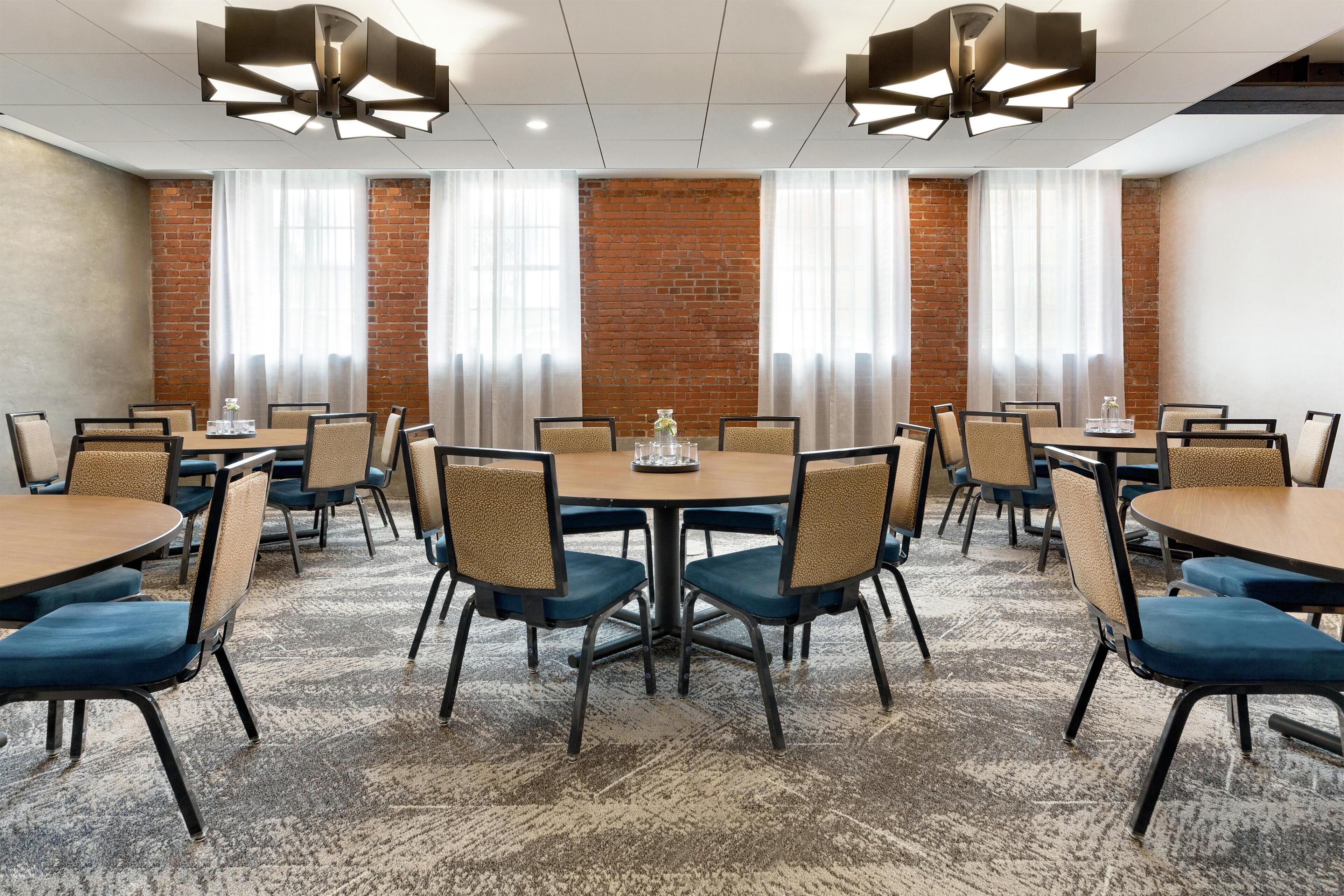 A conference room with round tables, chairs, and a brick wall.