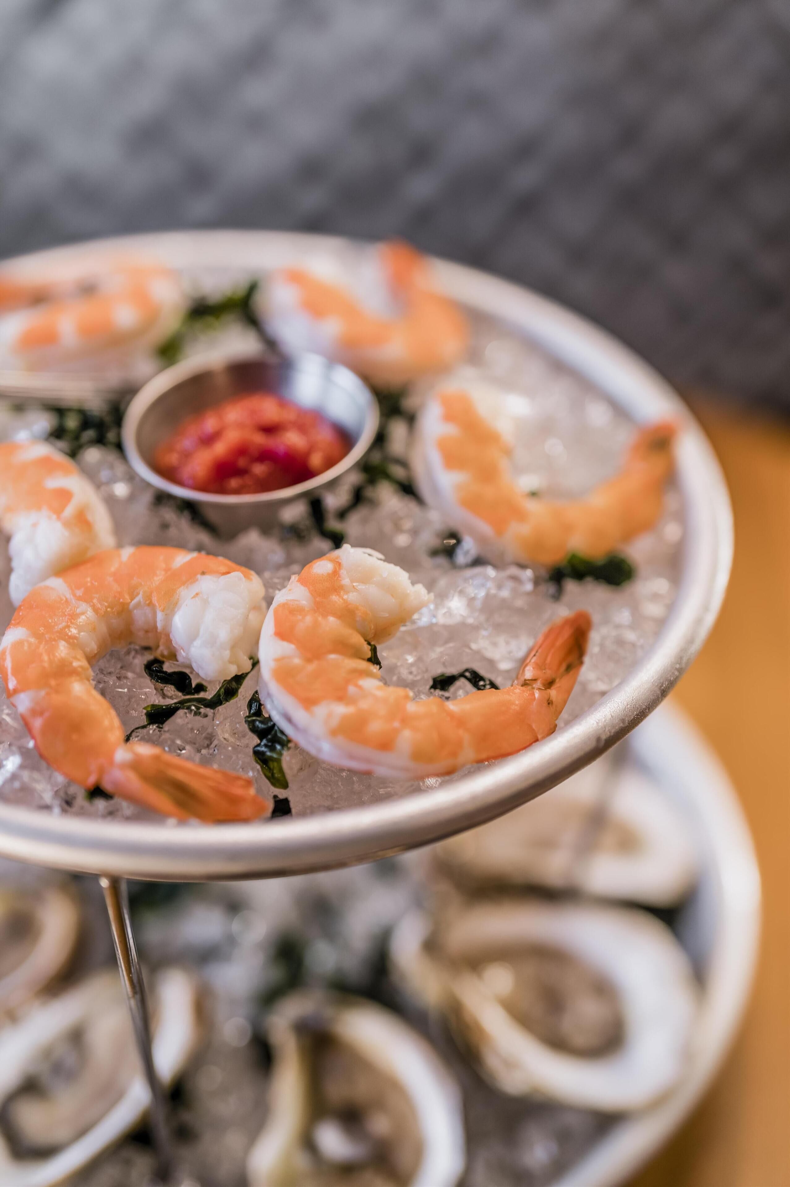 A plate of shrimp on ice with a small bowl of sauce.
