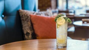 A glass of iced beverage with a lime slice and mint on a wooden table in a restaurant setting.