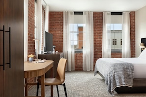 Une chambre d’hôtel comprenant un lit, un bureau avec une chaise, une télévision et une fenêtre avec des rideaux.