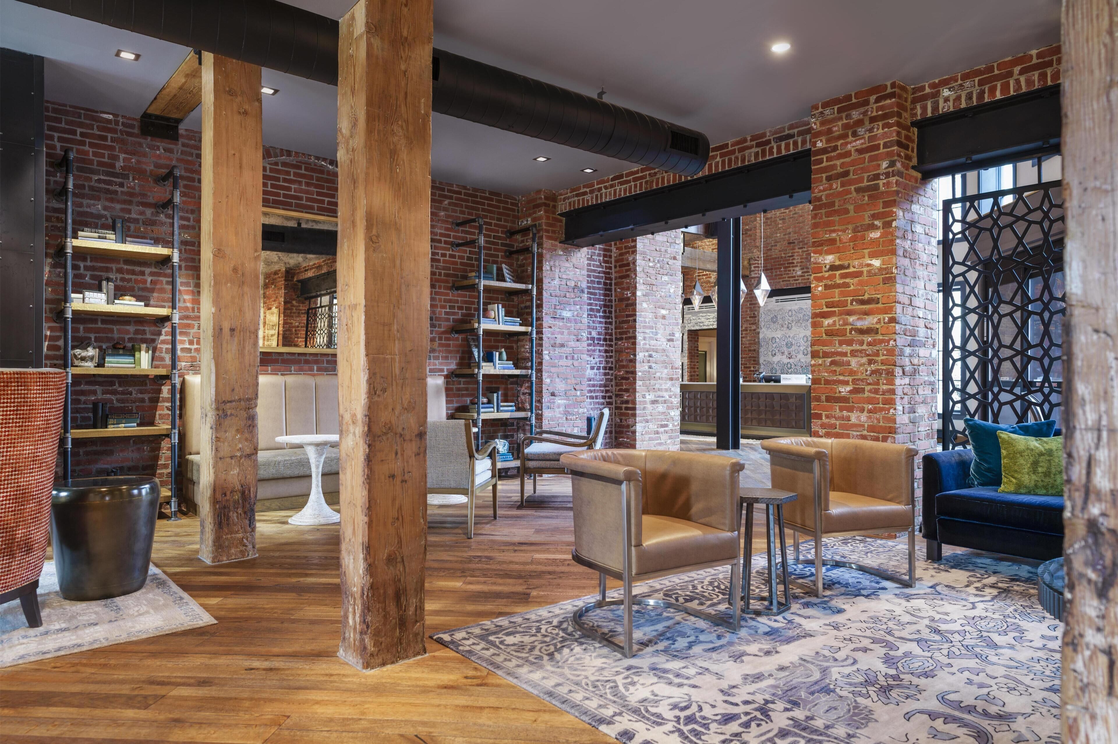 A spacious room with exposed brick walls, wooden beams, and a mix of seating areas including a sofa and chairs.