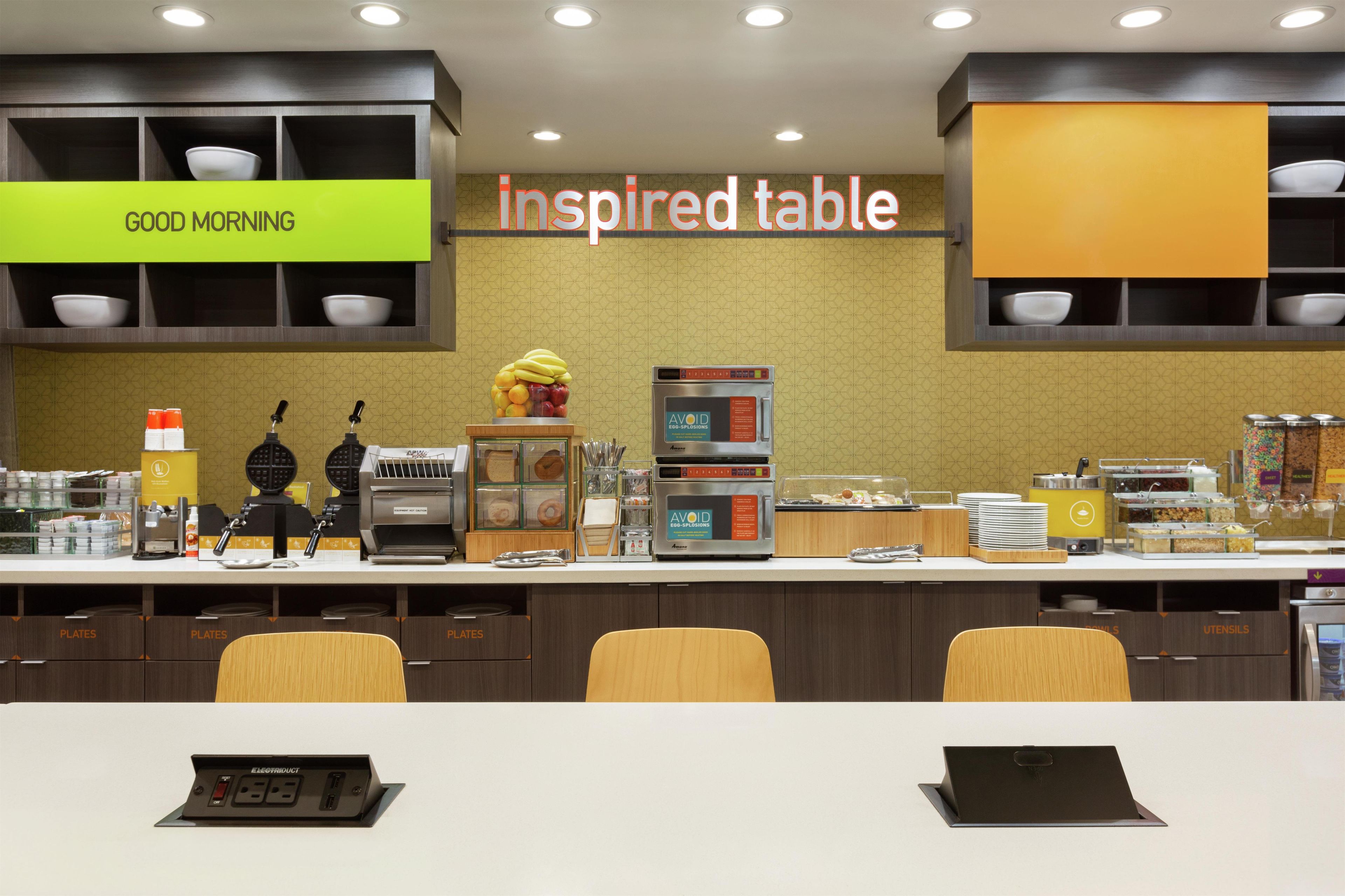 Un área de desayuno con un cartel que dice 'inspired table', una máquina de café y diversas opciones de comida.