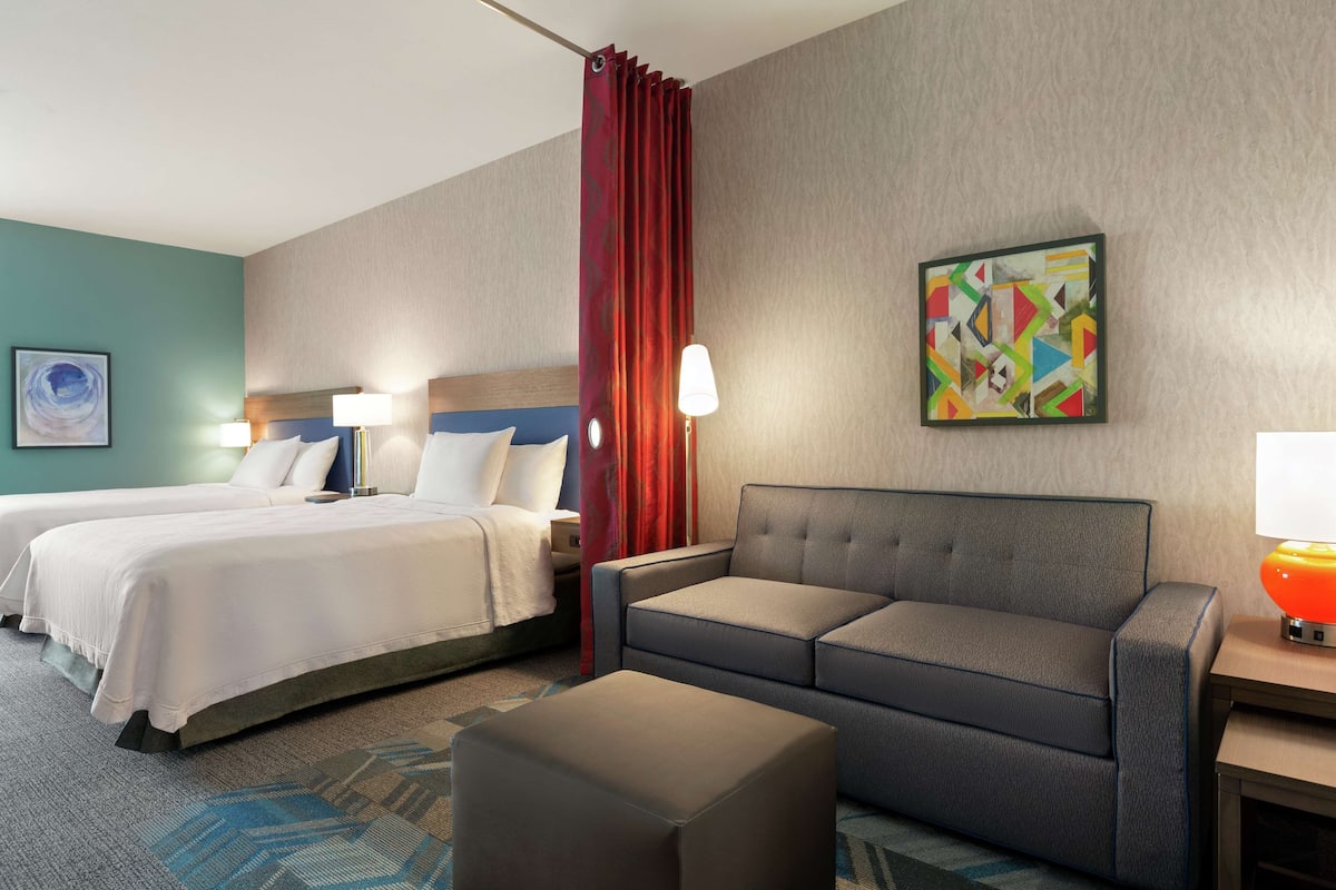 A hotel room with two beds, a sofa, a small table, and a lamp.