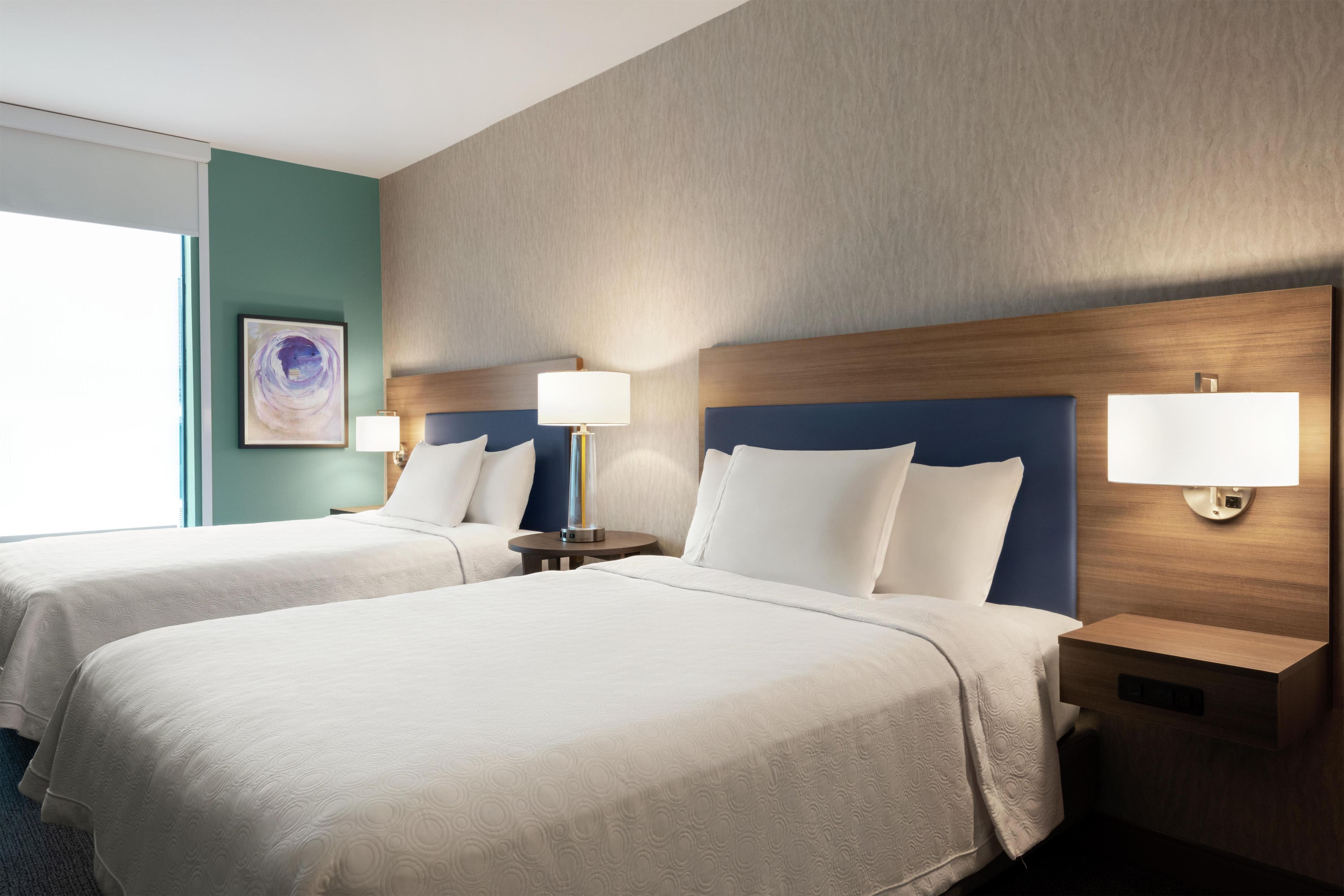 Une chambre d’hôtel avec deux lits, une tête de lit, des lampes de chevet, une lampe fixée au mur et une œuvre d’art encadrée.