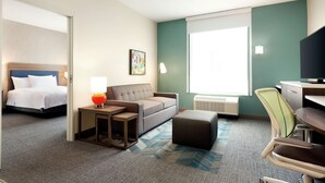 A hotel room with a bed, a sofa, a desk, a chair, and a window. - Home2 Suites by Hilton Houston-Pearland (Houston)