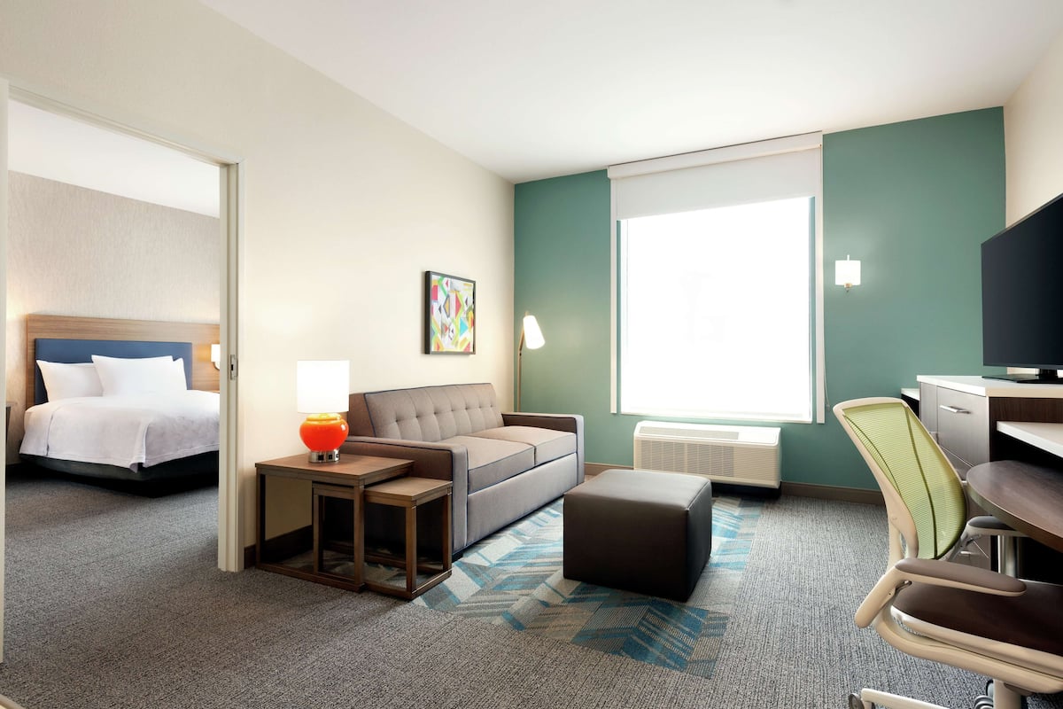 A hotel room with a bed, a sofa, a desk, a chair, and a window.