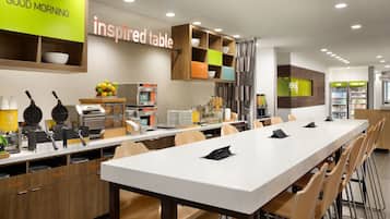 A modern breakfast area with a long table, seating, and a variety of breakfast items.