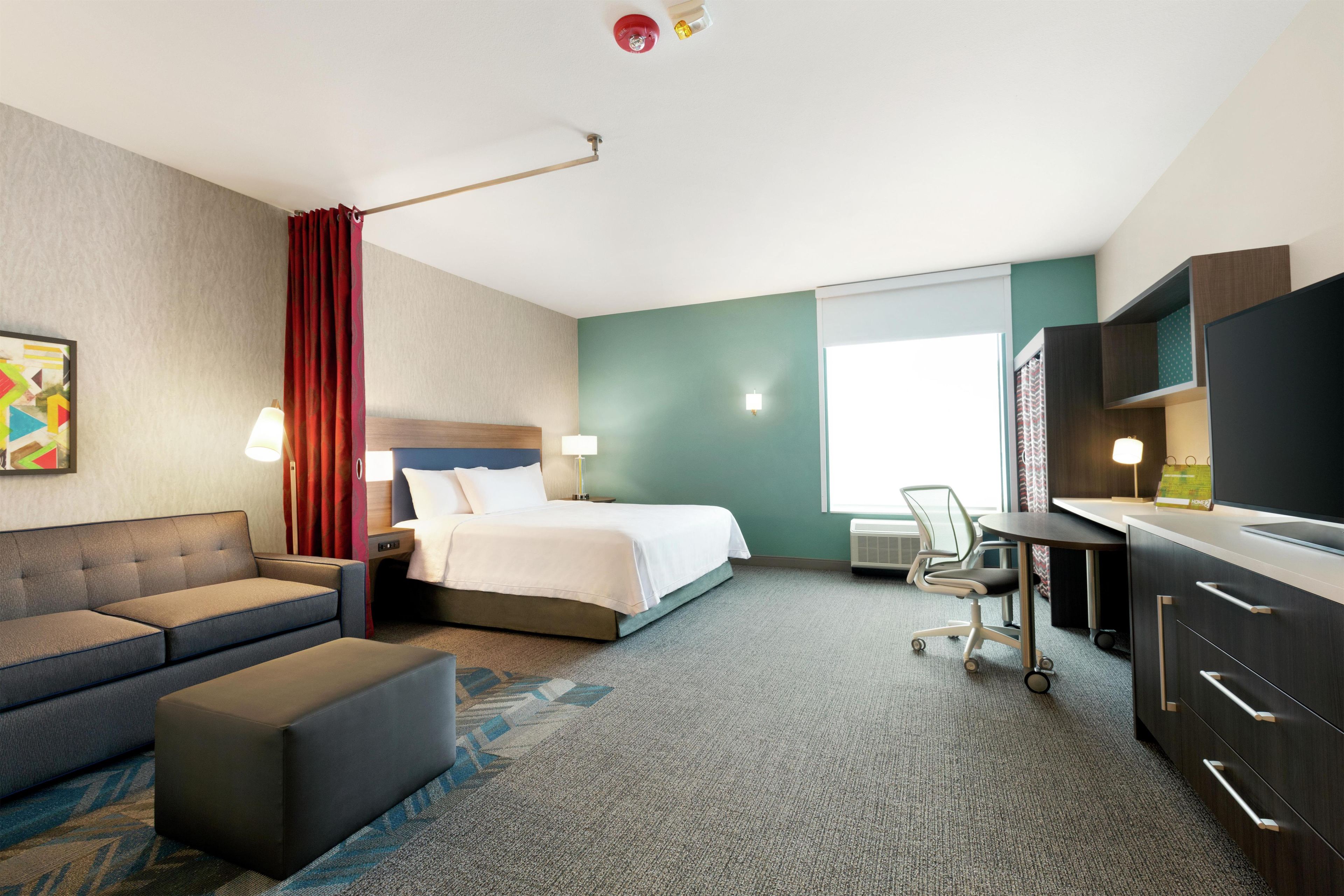A hotel room with a bed, a desk, a chair, a sofa, and a television.