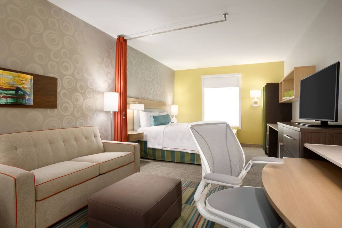 A hotel room with a bed, a sofa, a chair, a desk, and a television.