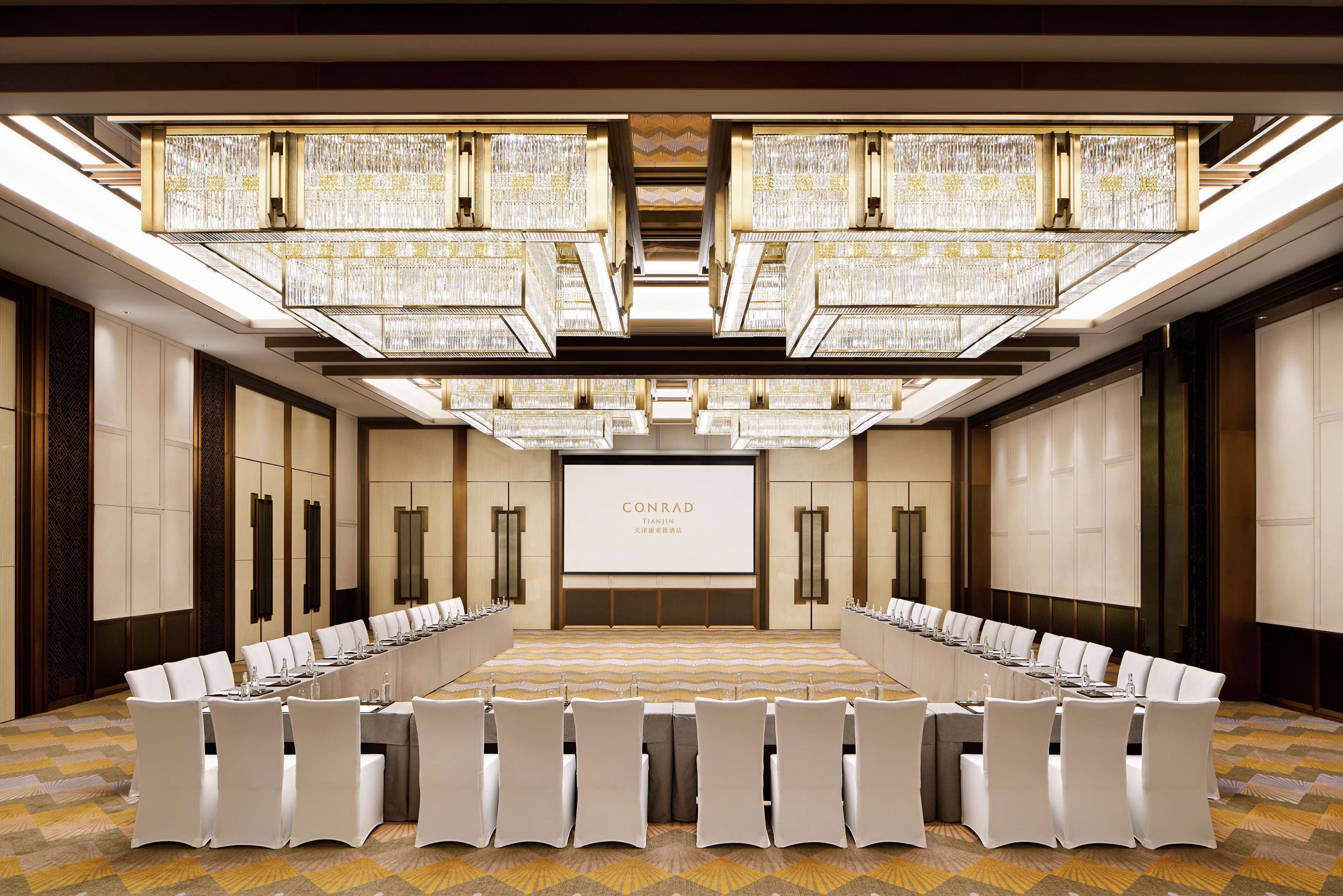 A conference room with a long table, white chairs, and a large screen displaying 'CONRAD'.