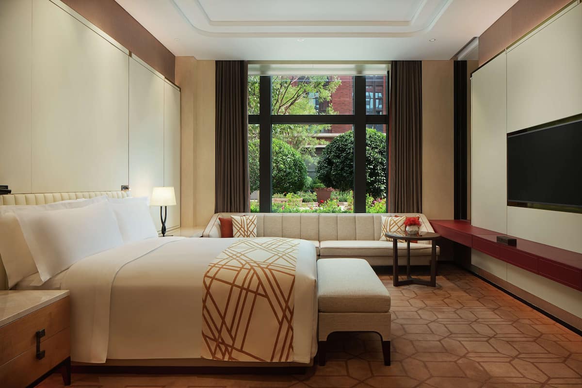 A hotel room with a large bed, a sofa, a small table, and a TV.