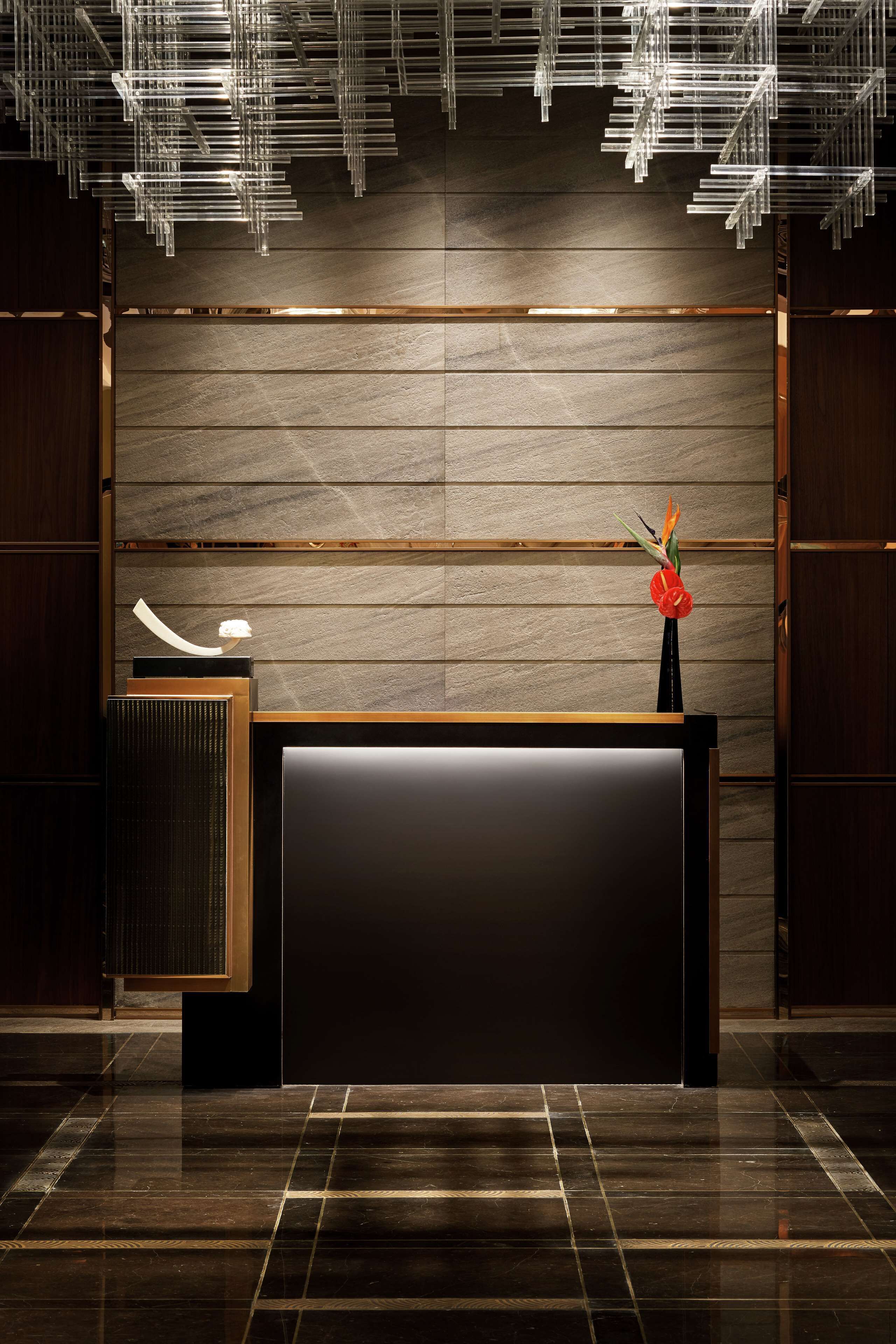 A modern reception desk with a dark surface, a wooden panel wall, and a decorative vase with flowers.