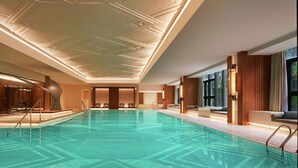 Una piscina interior con un diseño geométrico en el techo, paneles de madera y vistas al exterior a través de amplios ventanales.